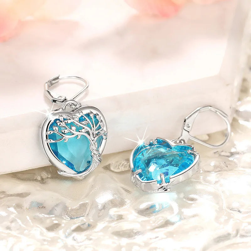 Blue crystal heart-shaped dangling earrings from Corporación Turística, featuring elegant, faceted crystal design.