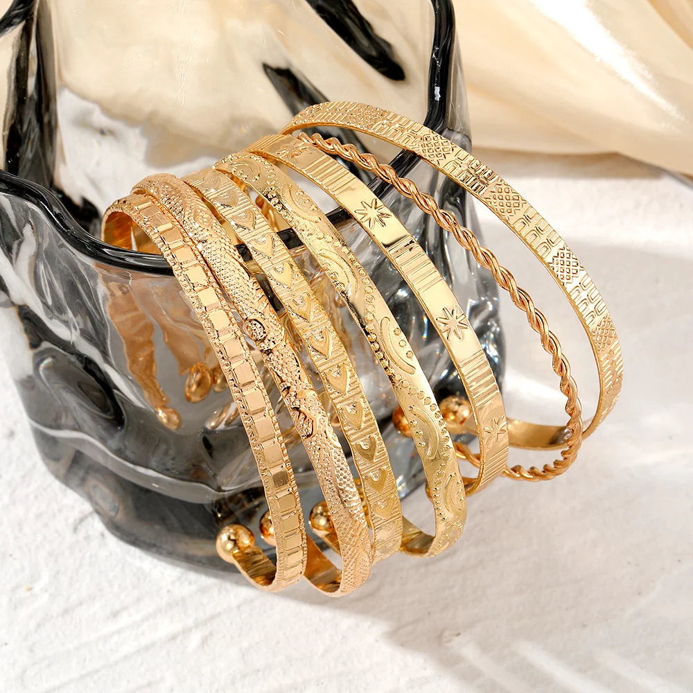 Set of 7 gold-colored punk-style bracelets for women, featuring various designs and textures, on a plain background.
