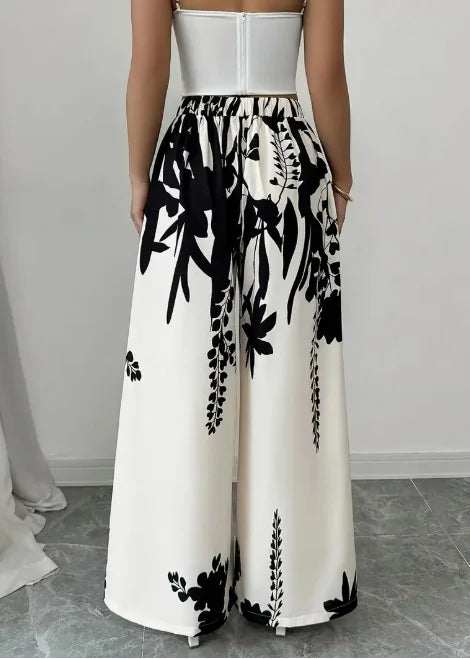 Wide-leg satin floral print pants by Corporación Turística, featuring smooth, shiny fabric and vibrant floral design.