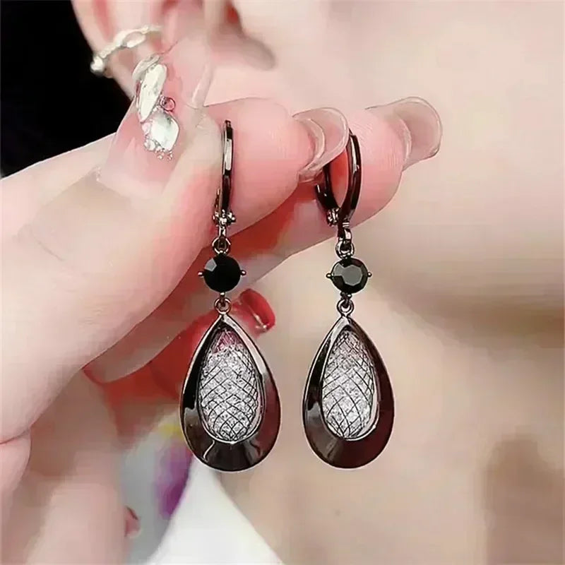 Exquisitos pendientes colgantes de cristal en forma de gota, blancos, de la marca Corporación Turística, con detalles brillantes y elegantes.