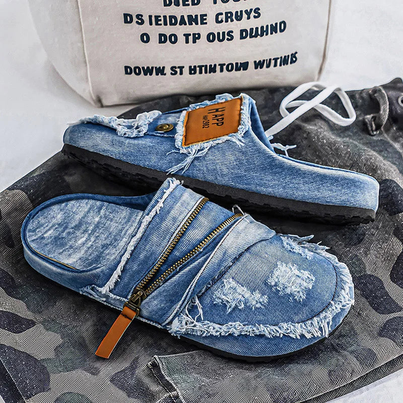 Light blue denim mules with frayed edges from Corporación Turística, showing the textured fabric and slip-on design.