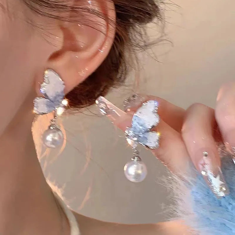 Crystal and pearl butterfly dangle earrings from Corporación Turística, featuring delicate hanging design with vibrant purple accents.