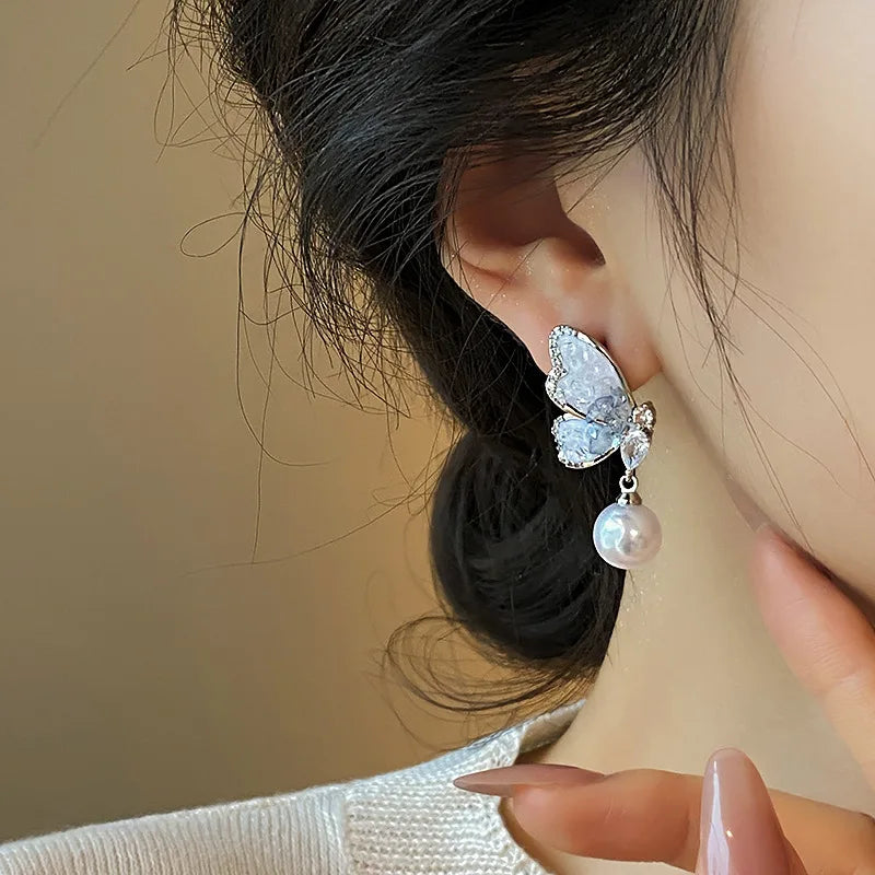 Crystal and pearl butterfly drop earrings from Corporación Turística, featuring delicate dangling design with vibrant purple accents.