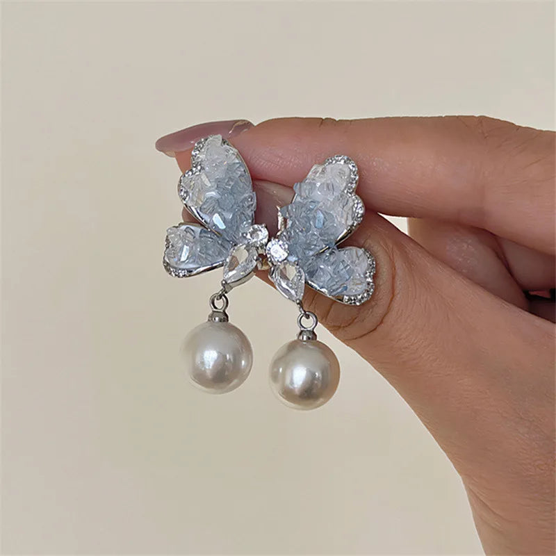 Elegant butterfly pendant earrings with crystal and pearl accents, featuring dangling design from Corporación Turística.