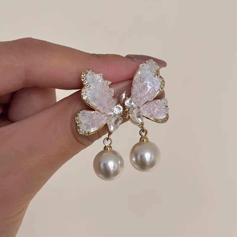 Crystal and pearl butterfly pendant earrings, elegant jewelry with dangling design, featuring vibrant purple hues and intricate details.