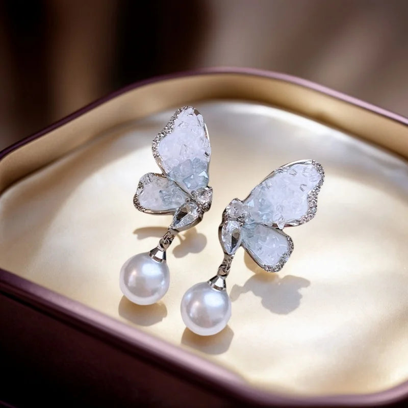 Crystal and pearl butterfly pendant earrings from Corporación Turística, featuring delicate hanging design and vibrant purple accents.