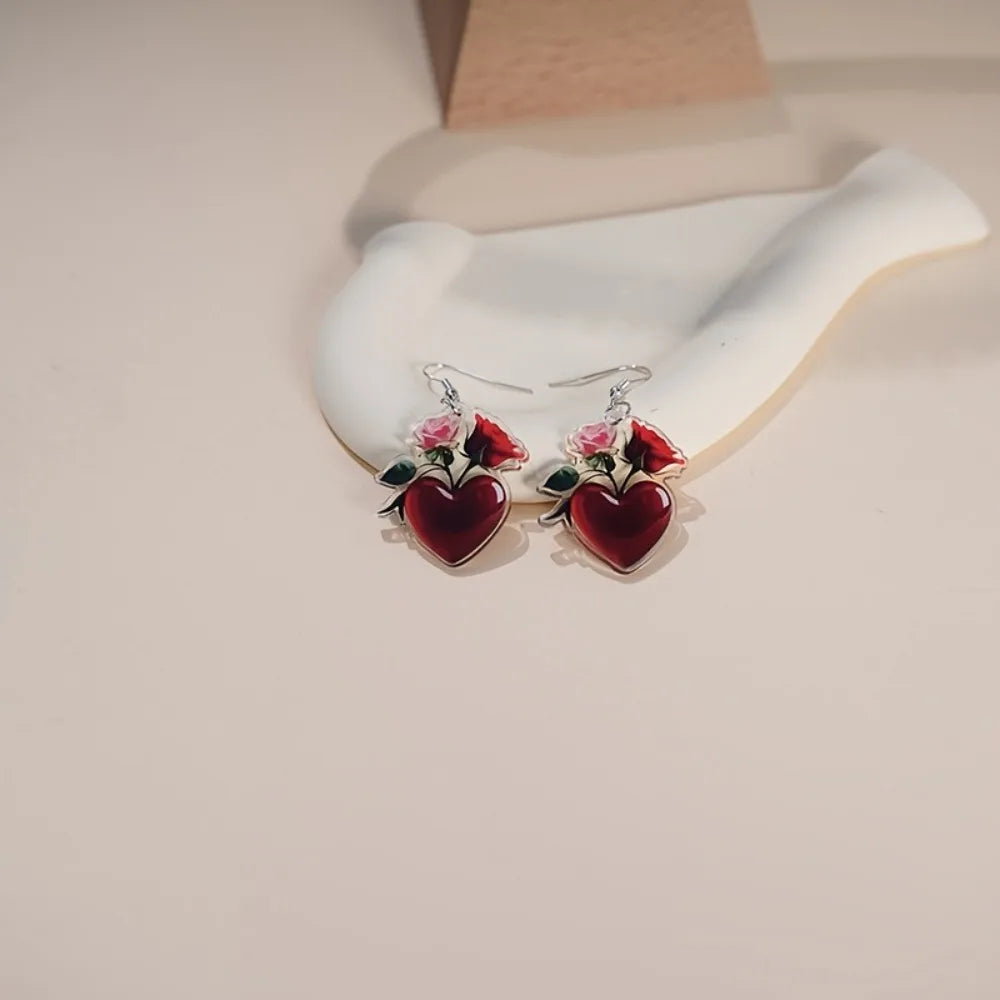 Acrylic heart-shaped dangling earrings from Corporación Turística, featuring vibrant red heart pendants with silver hooks.
