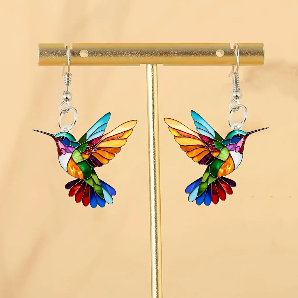 Acrílicos pendientes de colibrí con forma de pájaro colorido, diseñados por Corporación Turística, sobre fondo blanco.