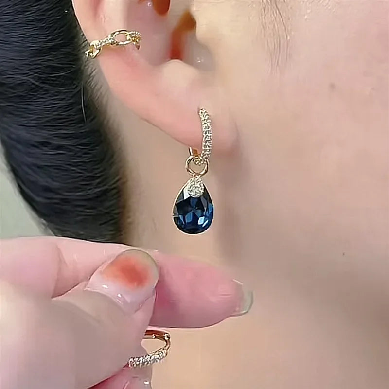 Exquisitos pendientes colgantes de cristal en forma de gota, diseñados por Corporación Turística, con acabado en color blanco.