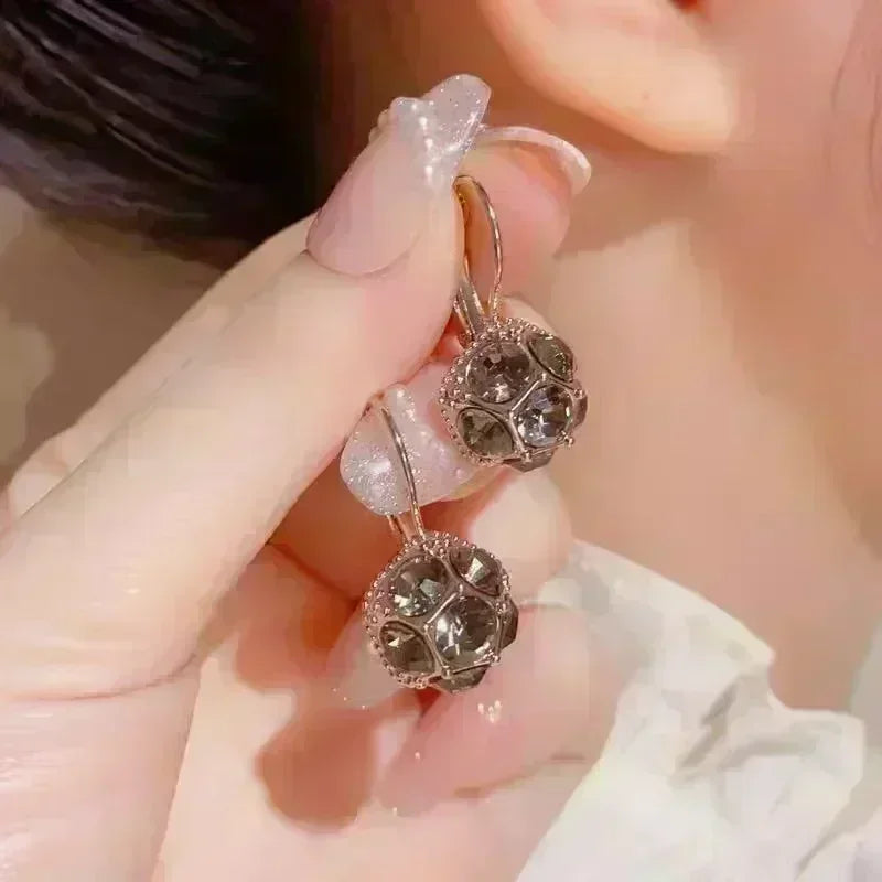 Elegant crystal drop earrings with teardrop-shaped pendants from Corporación Turística, featuring a sleek white finish.