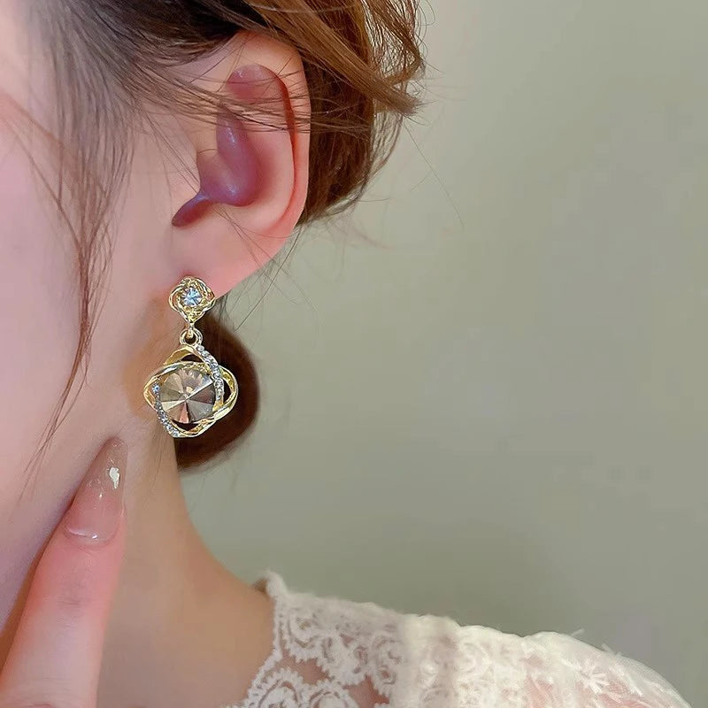 Elegant earrings with round crystal pendants wrapped in decorative wire, showcasing sparkling, stylish jewelry from Corporación Turística.