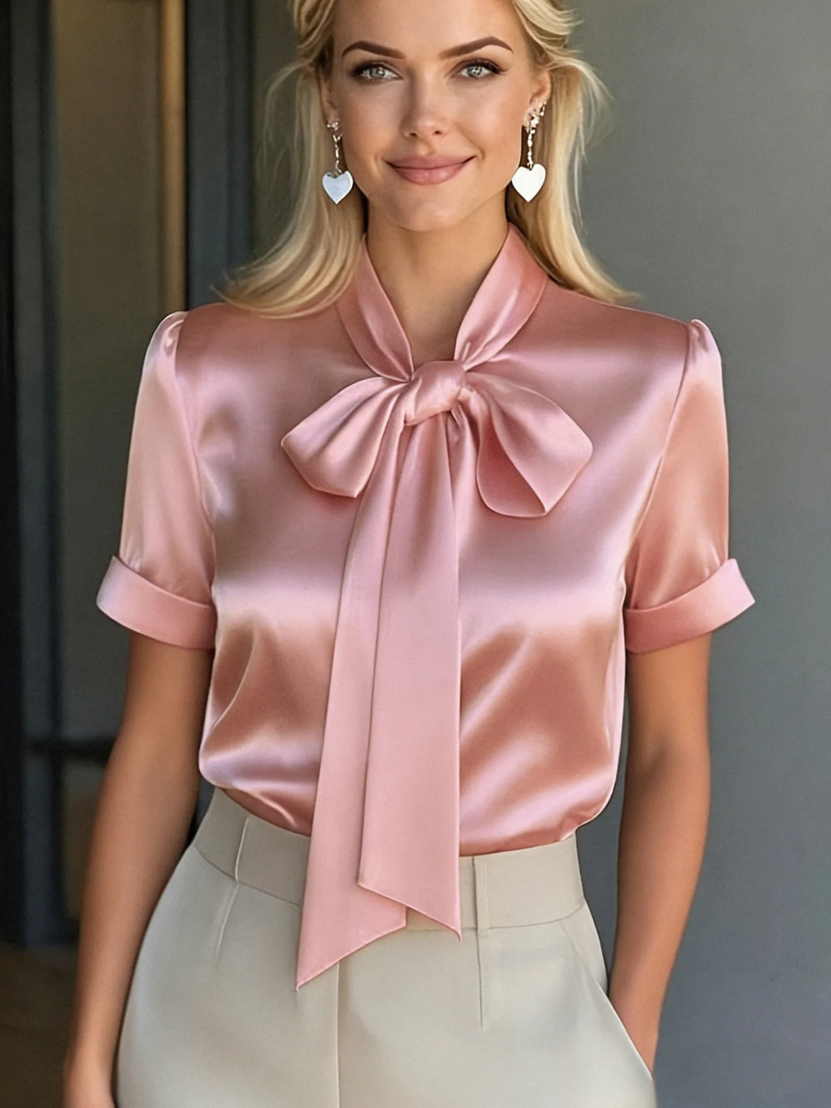 Short-sleeve satin bow blouse in apricot from Corporación Turística for 2026 fashion, shown on a hanger.