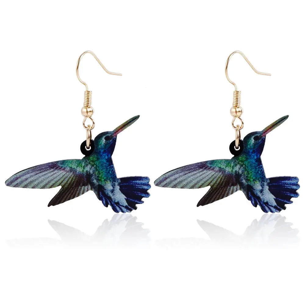 Acrílicos pendientes de colibrí de la marca Corporación Turística, con forma de colibrí colorido y moderno, en un fondo neutro.