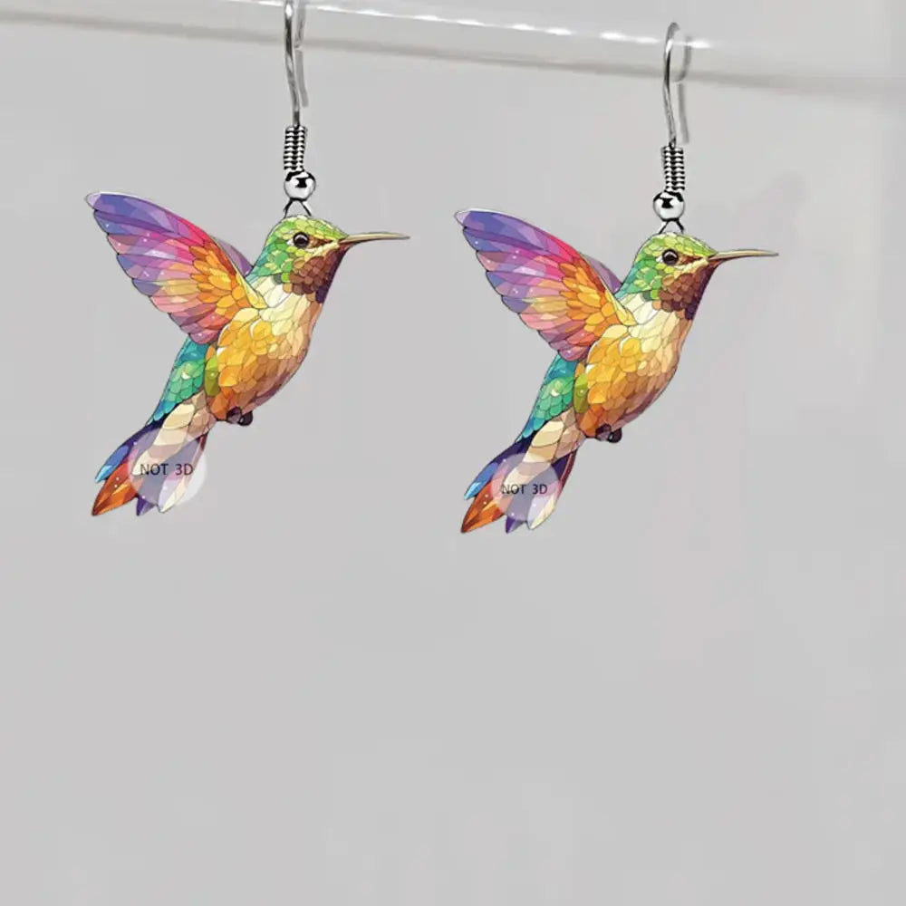 Acrylic hummingbird earrings with colorful, detailed bird-shaped design, crafted by Corporación Turística, hanging from silver hooks.