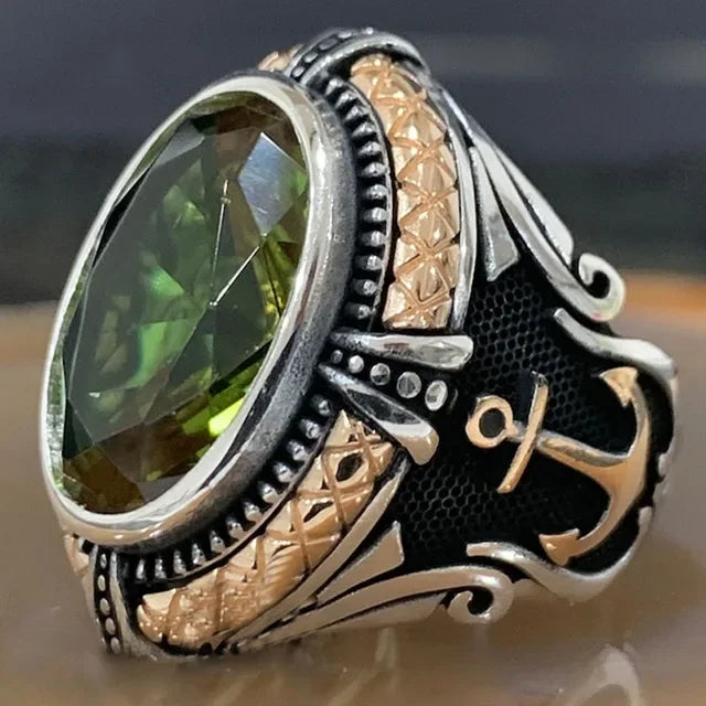 Luxurious green emerald ring with intricate inlays, crafted by Corporación Turística, displayed on a neutral background.